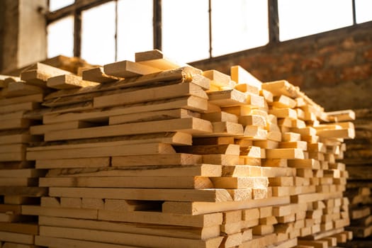 Stacked raw wooden planks at a indoor lumber warehouse. Background of boards. Raw wood drying in the lumber warehouse. Wood industry
