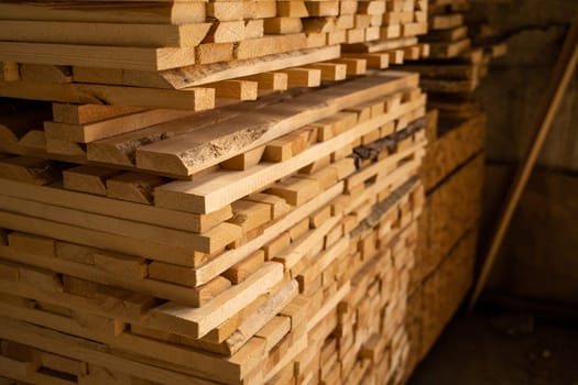 Raw stacked wooded planks drying in the lumber warehouse. Wooden planks in close-up. Background of boards. Wood timber stack of wooden blanks construction material. Industry