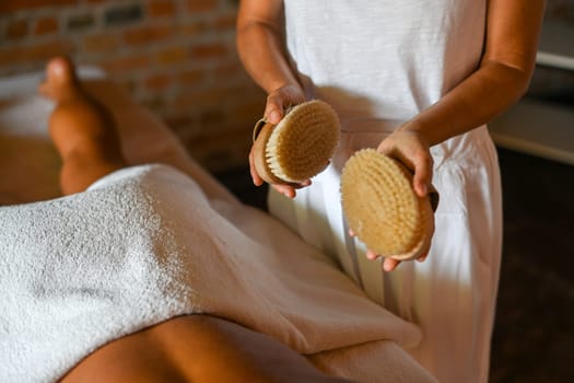 professional caucasian female physiotherapist masseuse performing brush massage to hispanic latino brunette woman in spa clinic