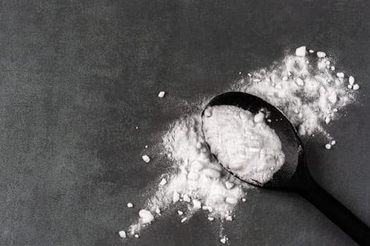 Baking soda, black spoon on grey wooden table, flat lay. Space for text