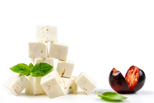 Feta cheese cubes isolated on white background with clipping path. Heap of Feta cheese, basil leaves and tomatoes.