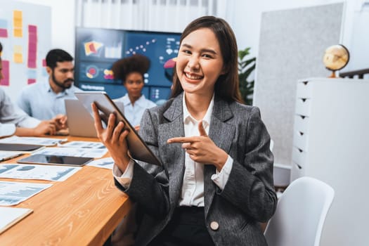 Portrait of happy young asian businesswoman with group of office worker on meeting with screen display business dashboard in background. Confident office lady at team meeting. Concord