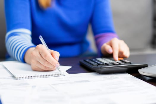 Woman using calculator for calculate domestic bills at home, doing paperwork for paying taxes