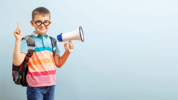 Little schoolboy with megaphone on blue background. Boy with megaphone making an announcement with copy space.