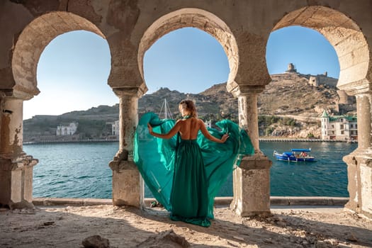 Woman dress sea columns. Rear view of a happy blonde woman in a long mint dress posing against the backdrop of the sea in an old building with columns