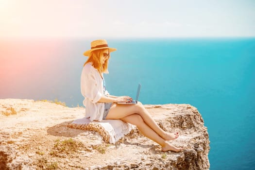 Freelance woman working on a laptop by the sea, typing away on the keyboard while enjoying the beautiful view, highlighting the idea of remote work