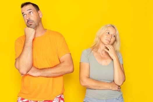 Contemplation of two lovers caucasian 40s couple spouses wife and husband boyfriend and girlfriend looking upwards, planning for future, thoughtful and pensive people isolated in yellow.