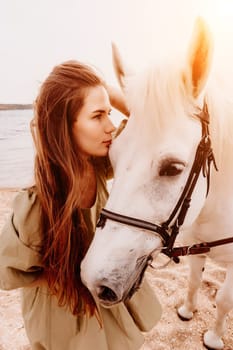 A woman in a dress stands next to a white horse on a beach, with the blue sky and sea in the background