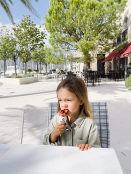 Little girl thoughtfully biting ice cream holding a waffle cone in her hand. High quality photo