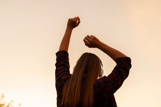 Silhouette of happy young woman in headphones enjoying music and dancing on a background of bright colorful sunset