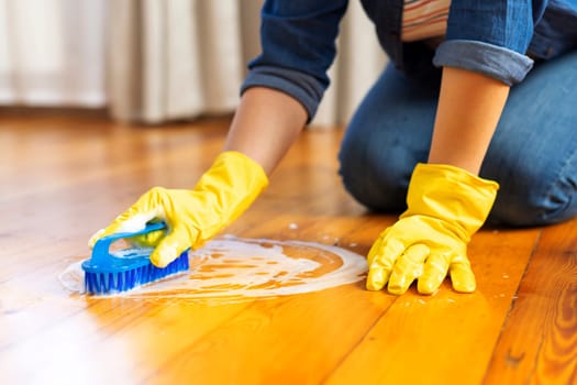 A young woman in protective gloves washes the floor with a brush and detergent. Cleaning service. Housework and housekeeping concept