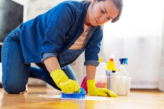 A young woman in protective gloves washes the floor with a brush and detergent. Cleaning service. Housework and housekeeping concept