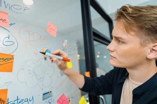 Closeup image of professional caucasian businessman presenting business idea with confident while writing and drawing mind map on glass board by using mind map and colorful sticky note. Immaculate.