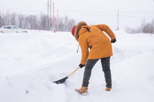 Young man clearing snow in his backyard village house with shovel. Remove snow from the sidewalk