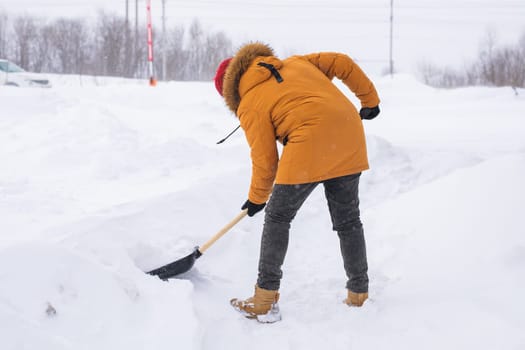 A man cleans and clears the snow in front of the house on frosty day. Cleaning the street from snow on a winter day. Snowfall and severe snowstorm in winter