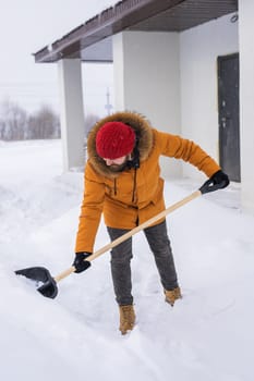 Young man clearing snow in his backyard village house with shovel. Remove snow from the sidewalk