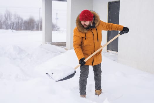 Young man clearing snow in his backyard village house with shovel. Remove snow from the sidewalk