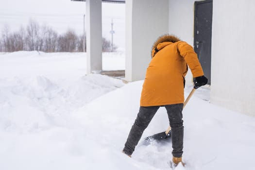 A man cleans and clears the snow in front of the house on frosty day. Cleaning the street from snow on a winter day. Snowfall and severe snowstorm in winter