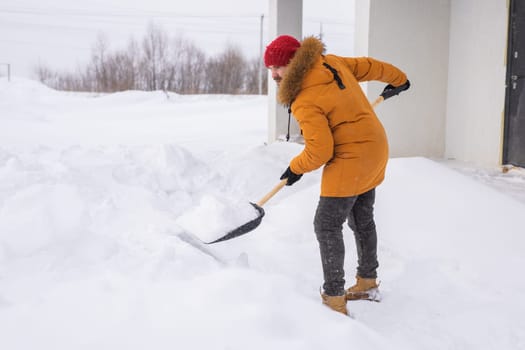 Young man clearing snow in his backyard village house with shovel. Remove snow from the sidewalk