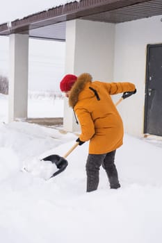 Young man clearing snow in his backyard village house with shovel. Remove snow from the sidewalk