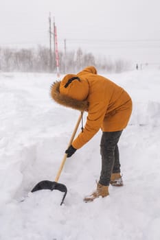 Young man clearing snow in his backyard village house with shovel. Remove snow from the sidewalk