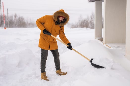 Young man clearing snow in his backyard village house with shovel. Remove snow from the sidewalk