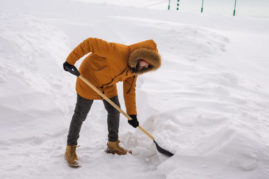 Young man clearing snow in his backyard village house with shovel. Remove snow from the sidewalk