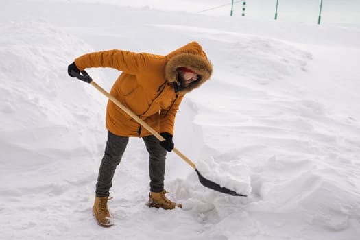 Young man clearing snow in his backyard village house with shovel. Remove snow from the sidewalk