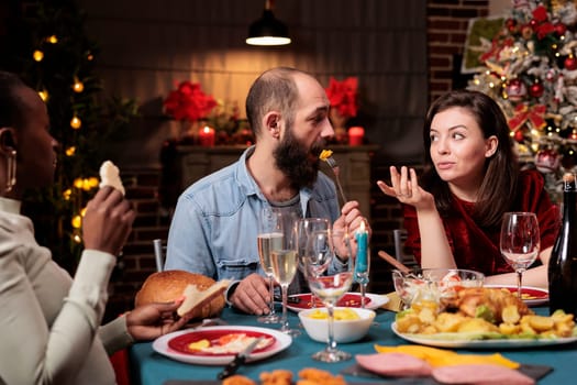 Couple celebrating christmas eve with family, acting romantic at dinner table with people. Diverse persons enjoying gathering with homemade food and alcohol to celebrate xmas holiday event.