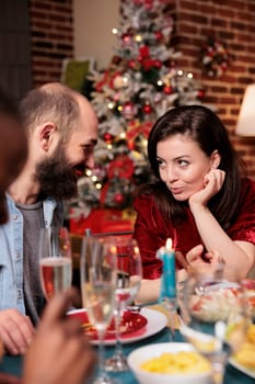 Cute couple enjoying christmas eve dinner with friends, celebrating holiday with traditional food. Diverse people gathering at home with family to eat and drink wine on xmas event.