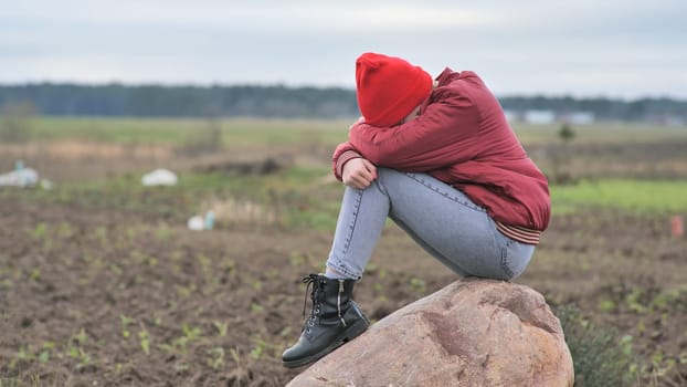 A sad teenage girl sits on a rock in a field and cries