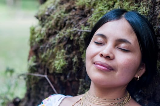 copy space close-up of an indigenous woman with her eyes closed resting on the bark of an ancient tree in the jungle of Ecuador, the woman feels peace and relaxation in the Amazon. Earth day. High quality photo