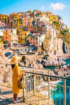 Asian woman with a hat looking out over Manarola Cinque Terre Italy, Manarola Village Cinque Terre Coast Italy. Manarola is a beautiful colorful town of La Spezia, Liguria one of the five Cinque Terre