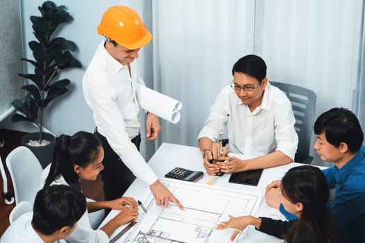 Diverse group of civil engineer and client working together on architectural project, reviewing construction plan and building blueprint at meeting table. Prudent