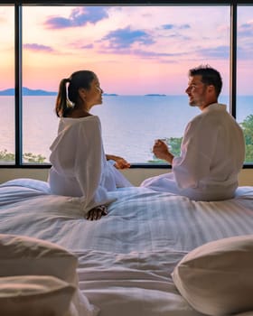 couple man and woman in front of the bed in a hotel bedroom during sunrise drinking a cup of coffee