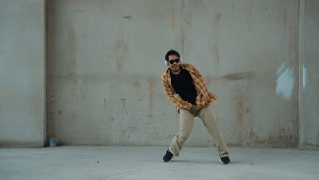 Attractive hispanic dancer in casual look practice street dance while listen music from headphone at cement background. Motion shot of break dancing performance. Outdoor sport 2024. Endeavor.