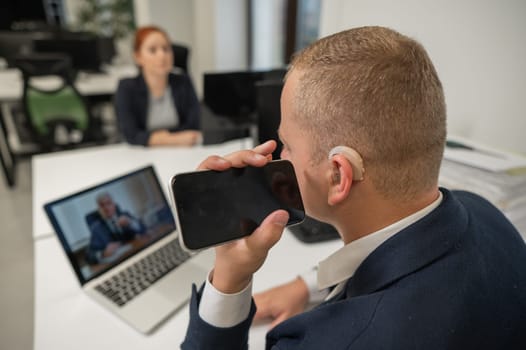 Caucasian man with a hearing aid talking on the phone on speakerphone