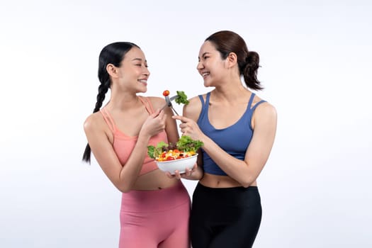 Two young sporty Asian women in sportswear holding salad bowl fill with fruit and vegetable. Natural youthful and fit body lifestyle people with balance nutrition on isolated background. Vigorous