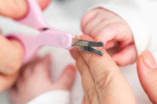 A close-up captures a mother attentively cutting her newborn's fragile nails with small scissors