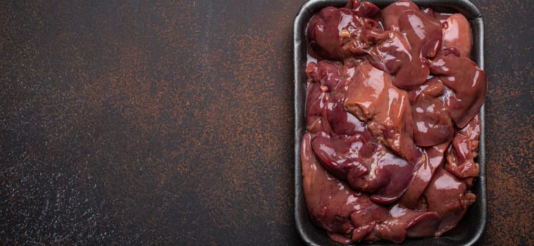 Raw chicken liver in black supermarket tray top view on dark rustic concrete background kitchen table. Healthy food ingredient, source of iron, folate, vitamins and minerals. Space for text