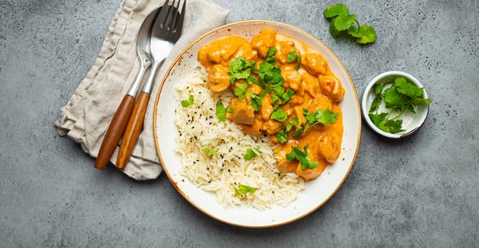 Traditional Indian dish chicken curry with basmati rice and fresh cilantro on rustic white plate on gray concrete table background from above. Indian dinner meal