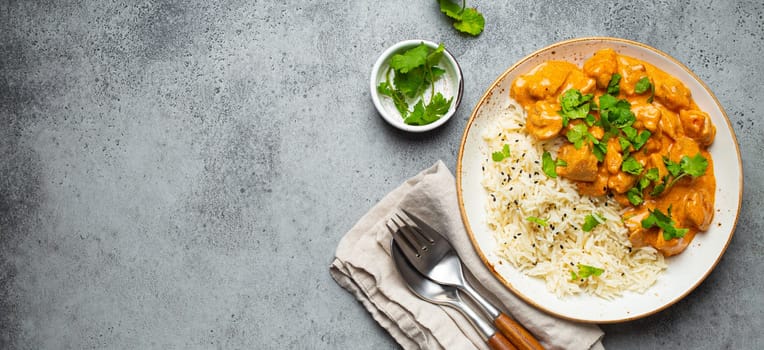 Traditional Indian dish chicken curry with basmati rice and fresh cilantro on rustic white plate on gray concrete table background from above. Indian dinner meal