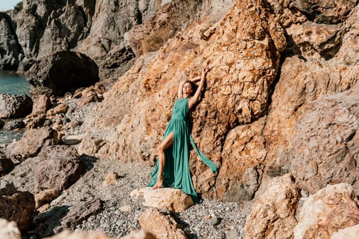 Woman green dress sea. Woman in a long mint dress posing on a beach with rocks on sunny day. Girl on the nature on blue sky background