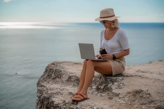 Freelance women sea working on the computer. Good looking middle aged woman typing on a laptop keyboard outdoors with a beautiful sea view. The concept of remote work