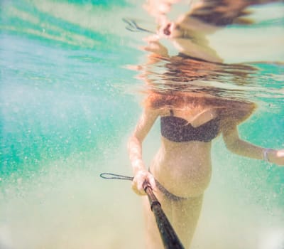 In an ethereal underwater scene, a pregnant woman gracefully floats, embodying the beauty of maternity beneath the tranquil surface of the sea.