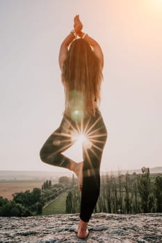 Well looking middle aged woman with long hair, fitness instructor in leggings and tops doing stretching and pilates on the rock near forest. Female fitness yoga routine concept. Healthy lifestyle.