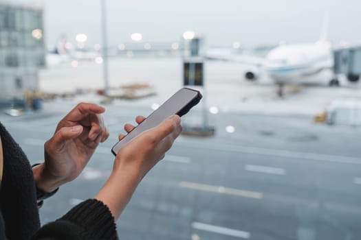 Happy Asian tourist uses mobile smartphone with travel backpack while waiting for flight in airport.