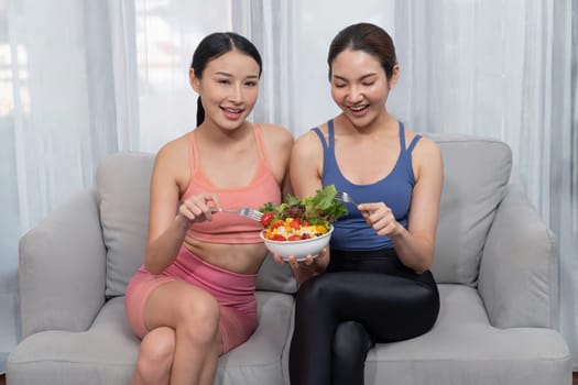 Young sporty Asian women in sportswear holding salad bowl together fill with vibrant of fruit and vegetable. Natural youthful and fit body lifestyle with balance nutrition and home exercise. Vigorous