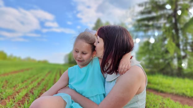 Happy mother and daughter enjoying rest, playing and fun on nature in green field. Woman and girl resting outdoors in summer or spring day