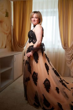 Portrait of beautiful elegant woman in in a royal dress indoors in nice room in evening time. Middle-aged adult lady in a romantic setting